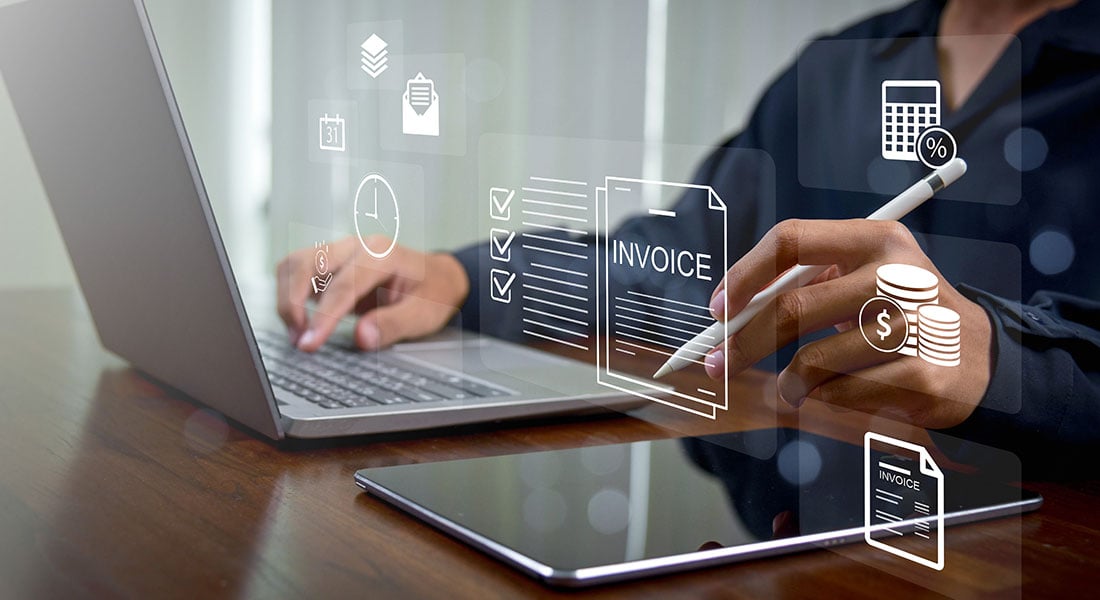 Business professional using a laptop and tablet with digital invoice and payment workflow graphics overlaid on the screen.
