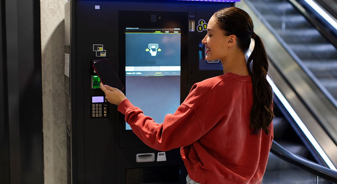woman using a smartphone to make a contactless payment at a parking kiosk